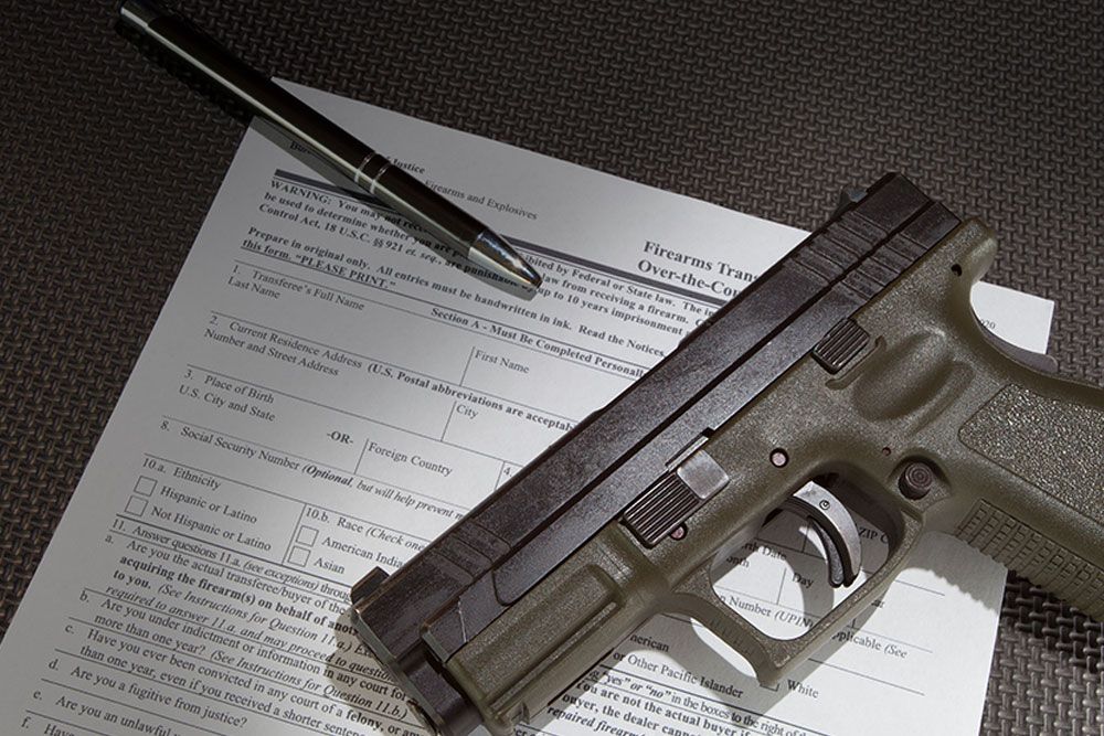 Handgun on top of firearm transaction paperwork with pen, symbolizing gun ownership and legal documentation process.