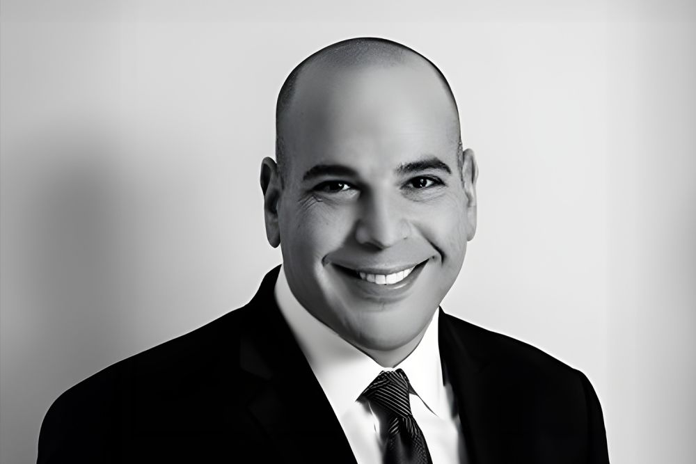 A smiling man in a suit and tie, black and white portrait against a neutral background.