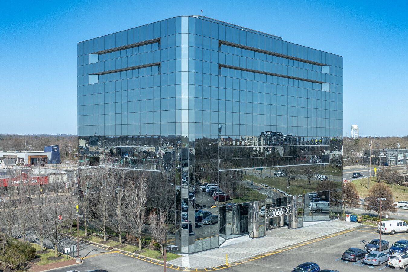Reflective glass office building with a modern facade and surrounding parking area under a clear blue sky.