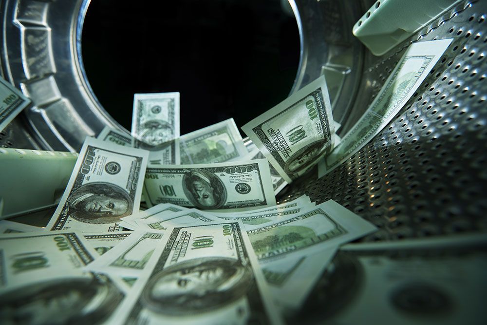 Hundred-dollar bills inside a metal washing machine, representing money laundering concept.