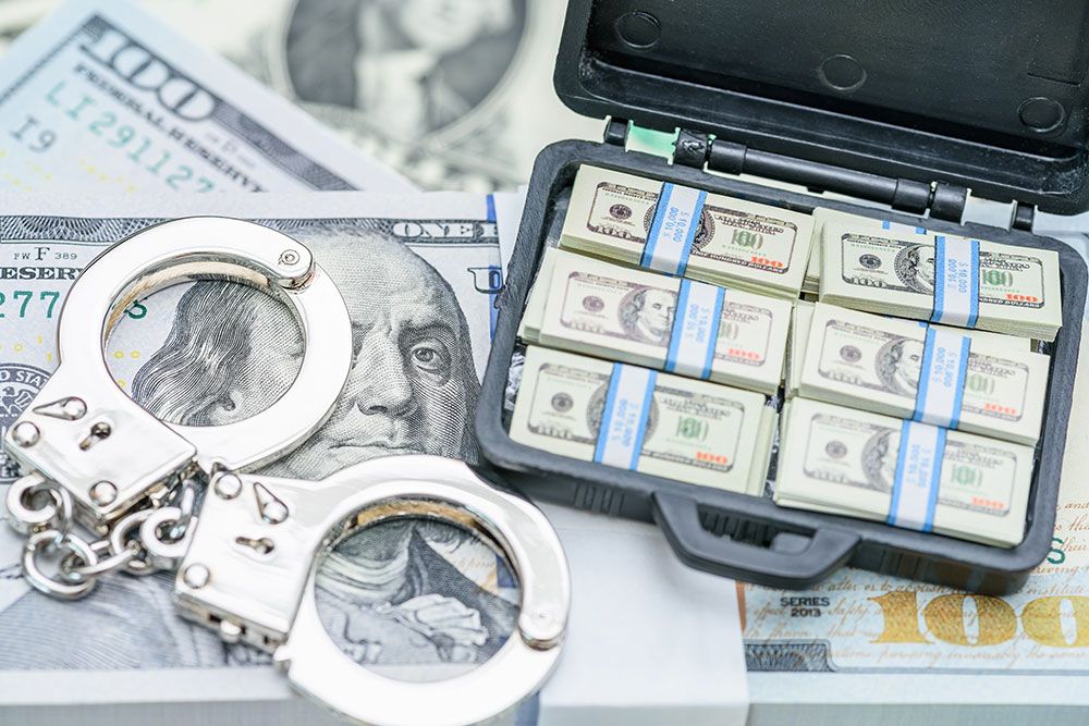 Stacks of hundred-dollar bills in a briefcase next to handcuffs, symbolizing financial crime or money laundering.