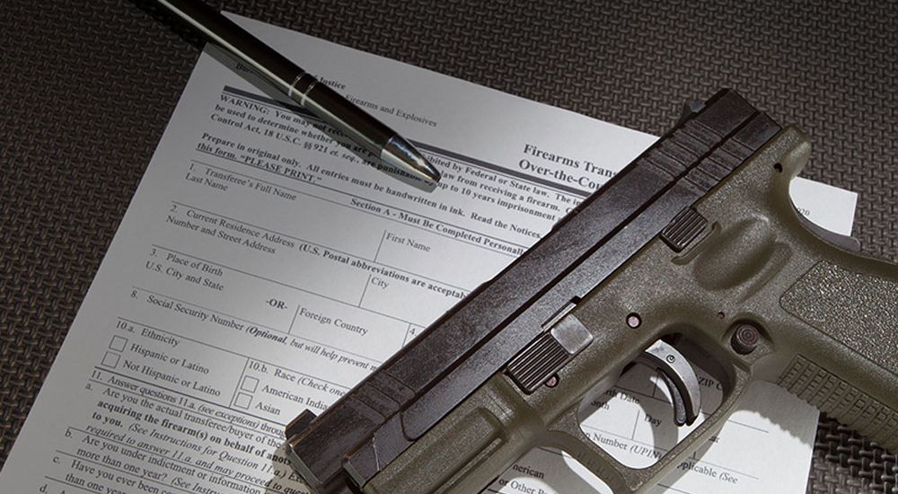 Handgun on top of firearm transaction paperwork with pen, symbolizing gun ownership and legal documentation process.