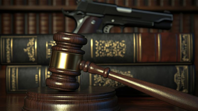 Gavel and law books with a handgun in the background, symbolizing legal issues related to firearms.