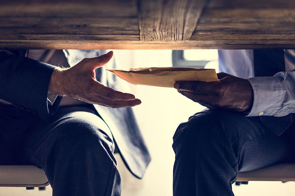 Two people discretely exchanging an envelope under a table, suggesting secrecy or a covert transaction.