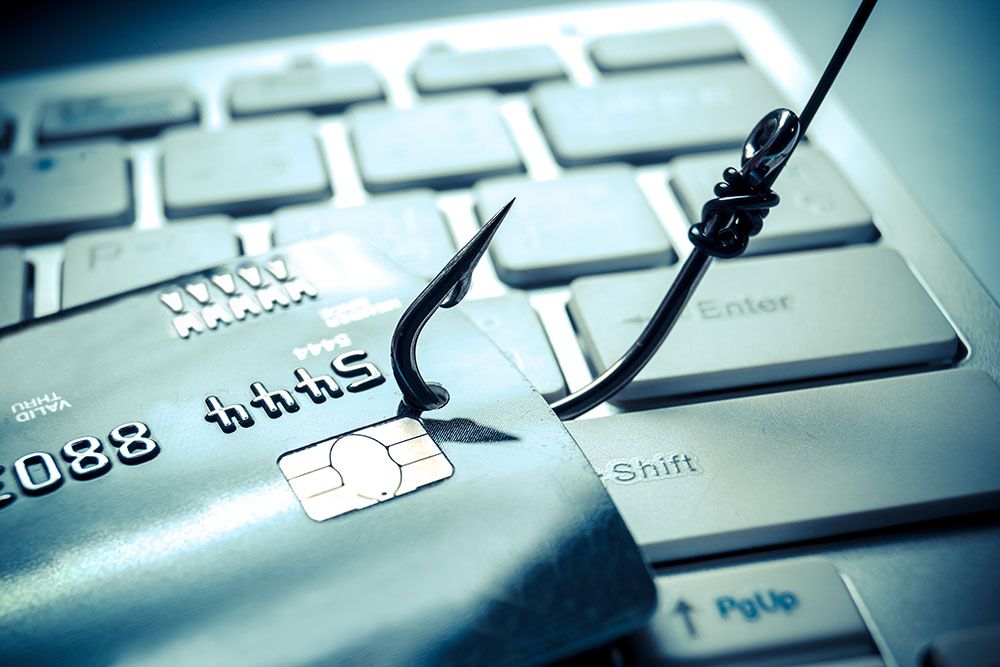 Credit card caught on fishing hook represents online phishing threat on a computer keyboard.
