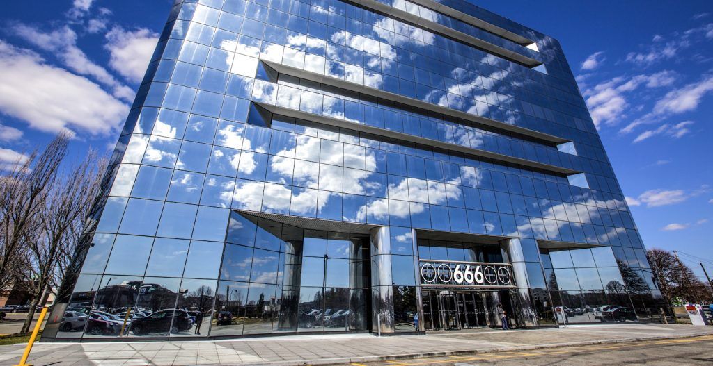 Modern glass building reflecting the sky with clouds, entrance marked by the number 666.