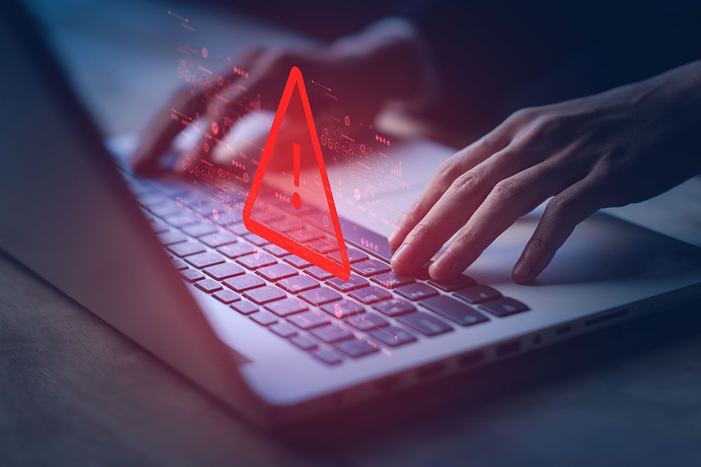 Hands typing on a laptop keyboard with a red warning symbol, indicating cyber threat or computer virus alert.