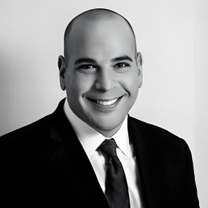 Portrait of a smiling man in a suit and tie, posing against a plain background.