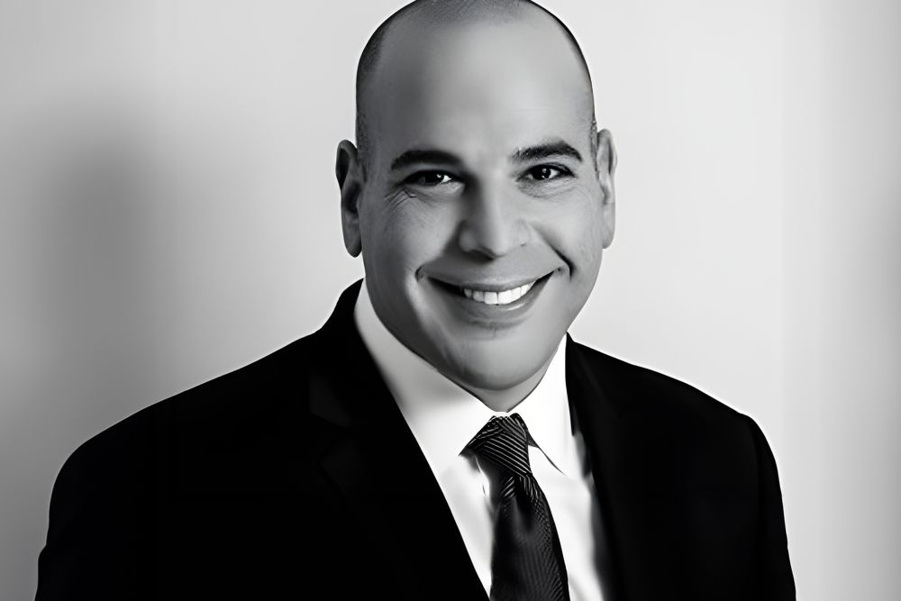 Smiling man in a suit and tie poses in a professional black-and-white portrait.