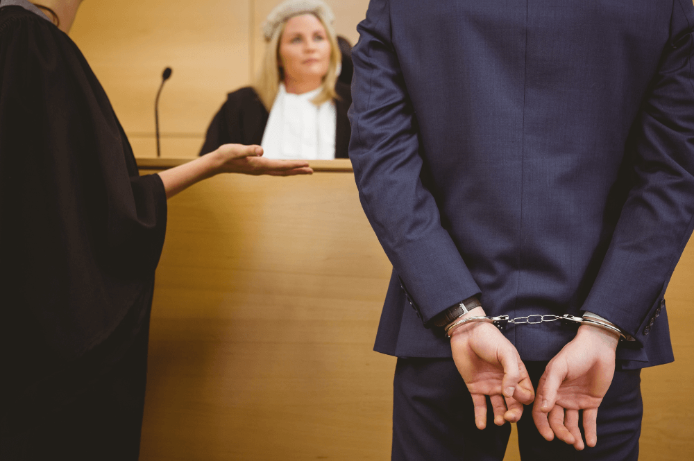 Defendant in handcuffs stands before judge in courtroom, legal proceeding in progress.