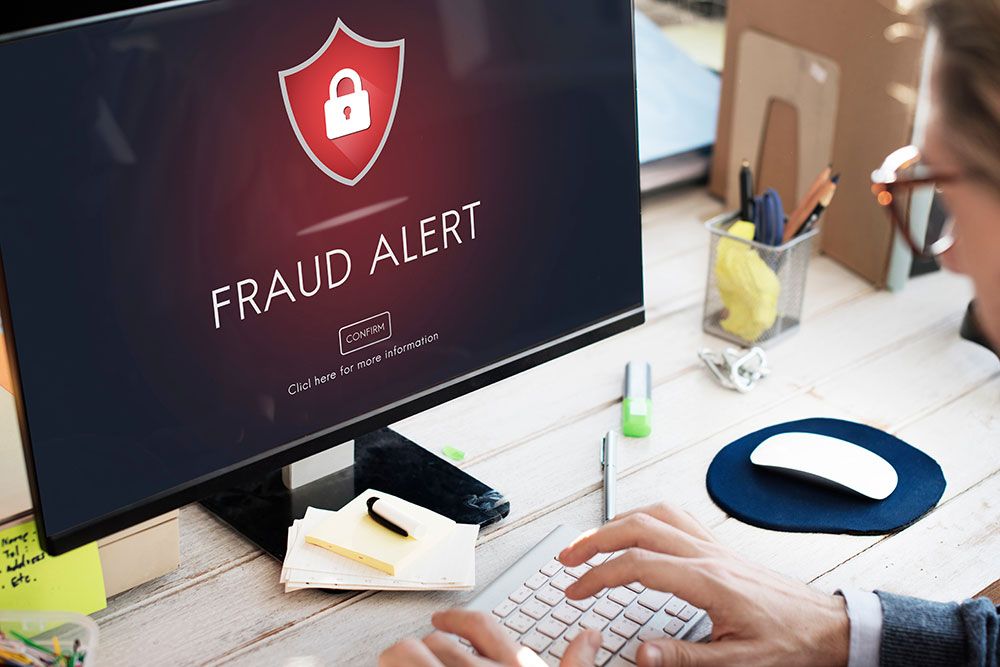 Fraud alert on computer screen with person typing at desk, focusing on cybersecurity warning.