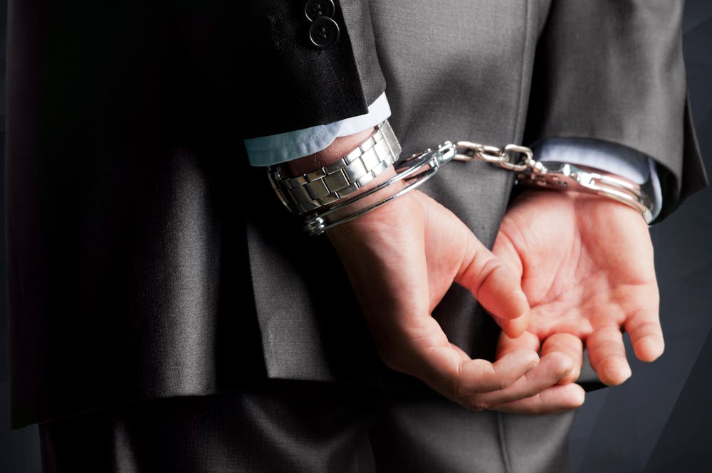 Person in business suit wearing handcuffs, symbolizing legal trouble or corporate crime consequences.