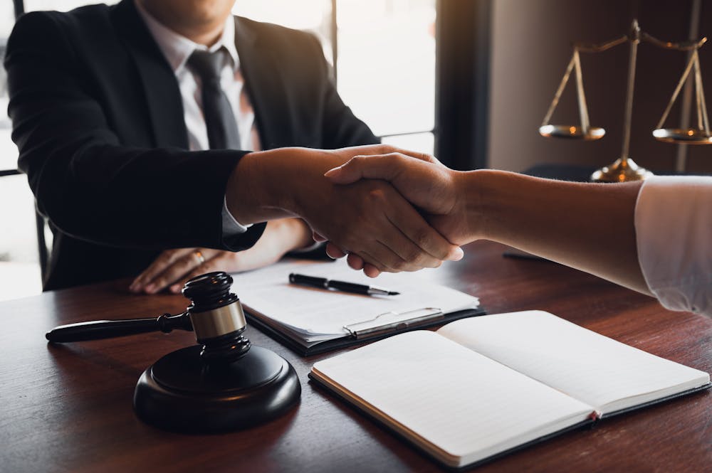 Handshake between two people in a legal office, symbolizing agreement, with a gavel and scales of justice nearby.